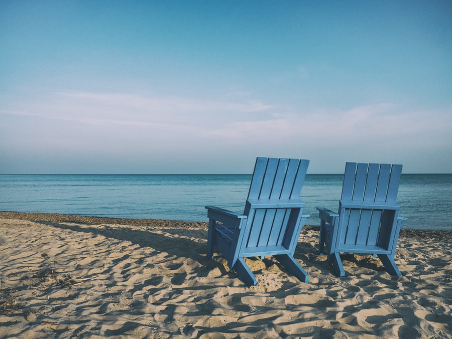 two lawnchairs on a beach facing the ocean
