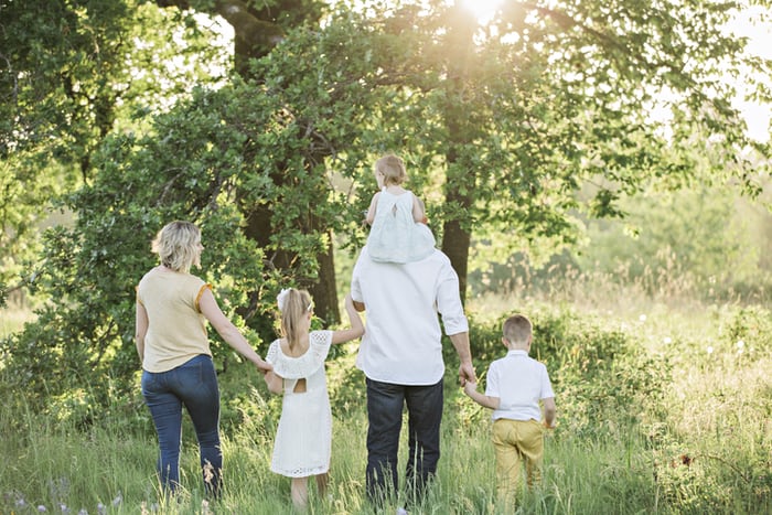 a family of four walking through the grass on a sunny day